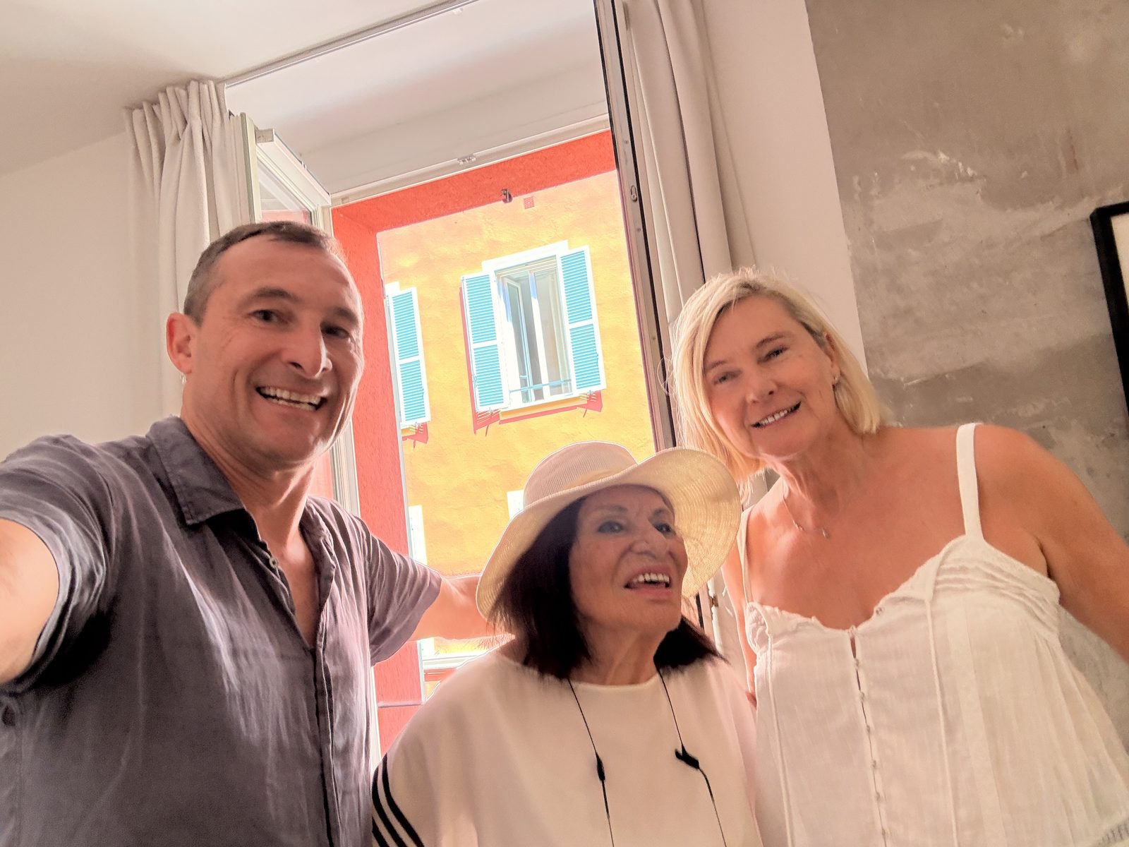 Three of the family in a doorway in Nice with bright pink and blue shutters behind
