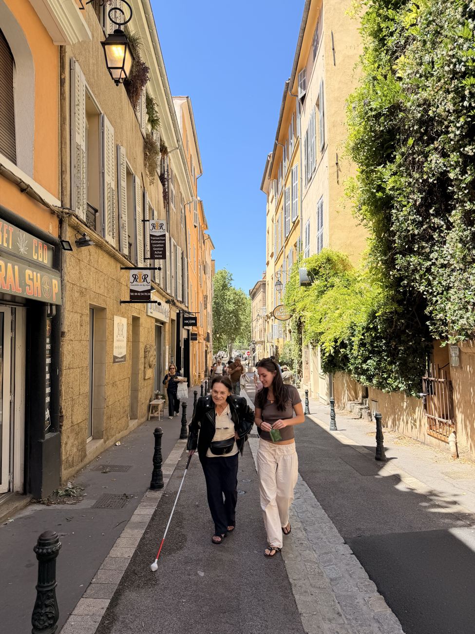 A narrow, sunlit street of Cannes' old town climbing between tall ochre houses, people walking up