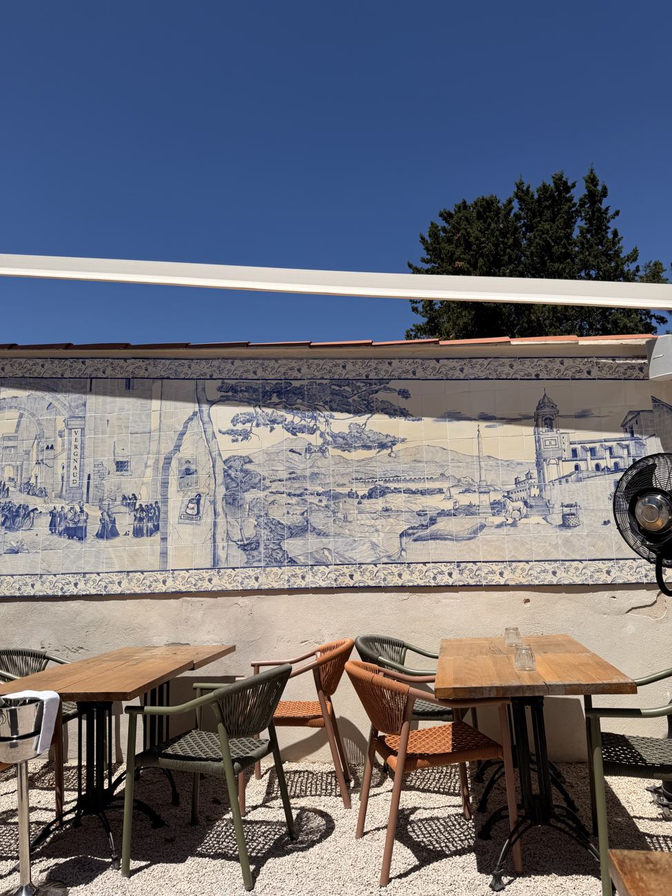 A restaurant terrace in Cannes with a painted azulejo tile mural and a view over the town