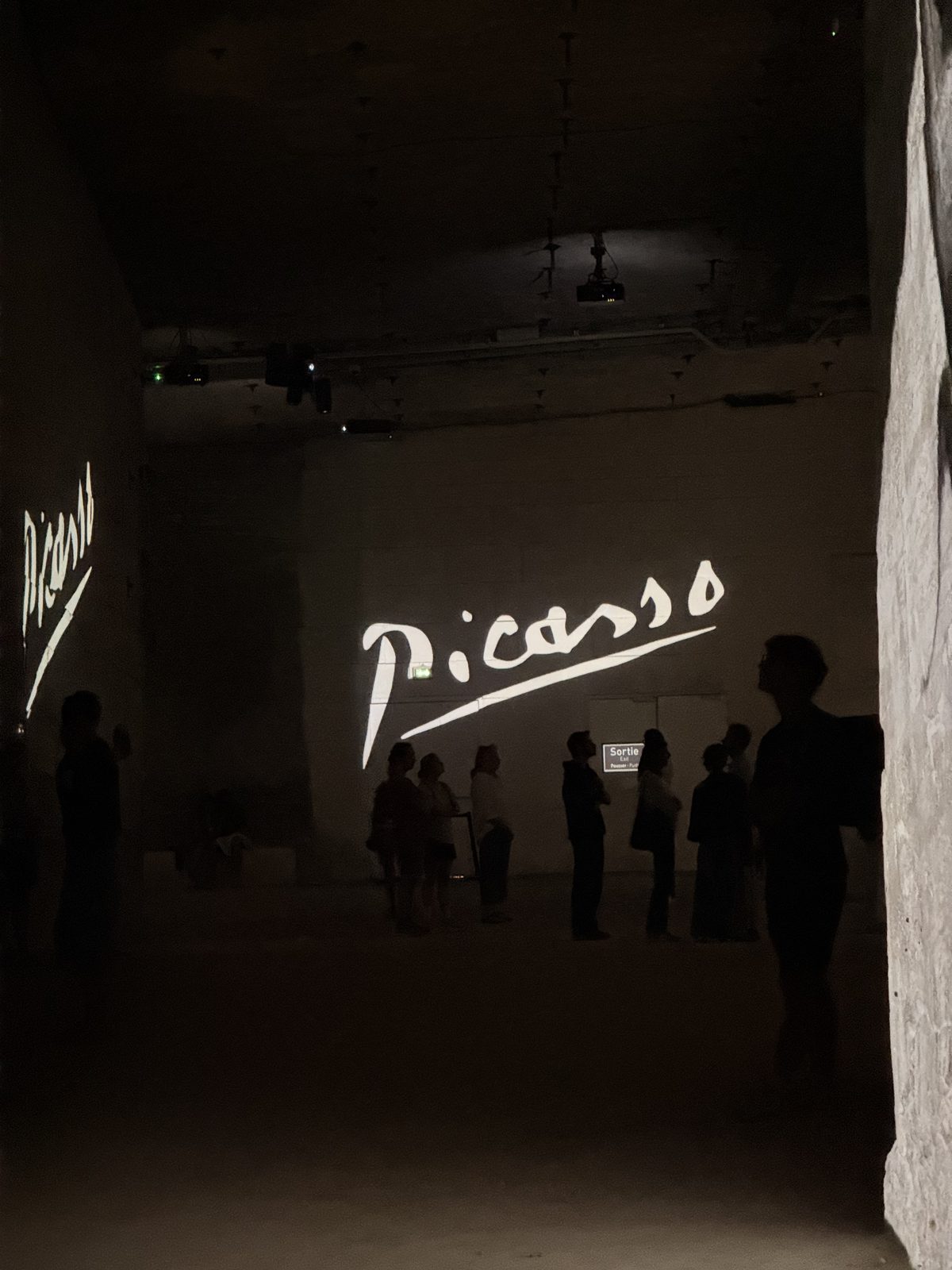 The word Picasso in white script on a dark wall at the entrance to the exhibition