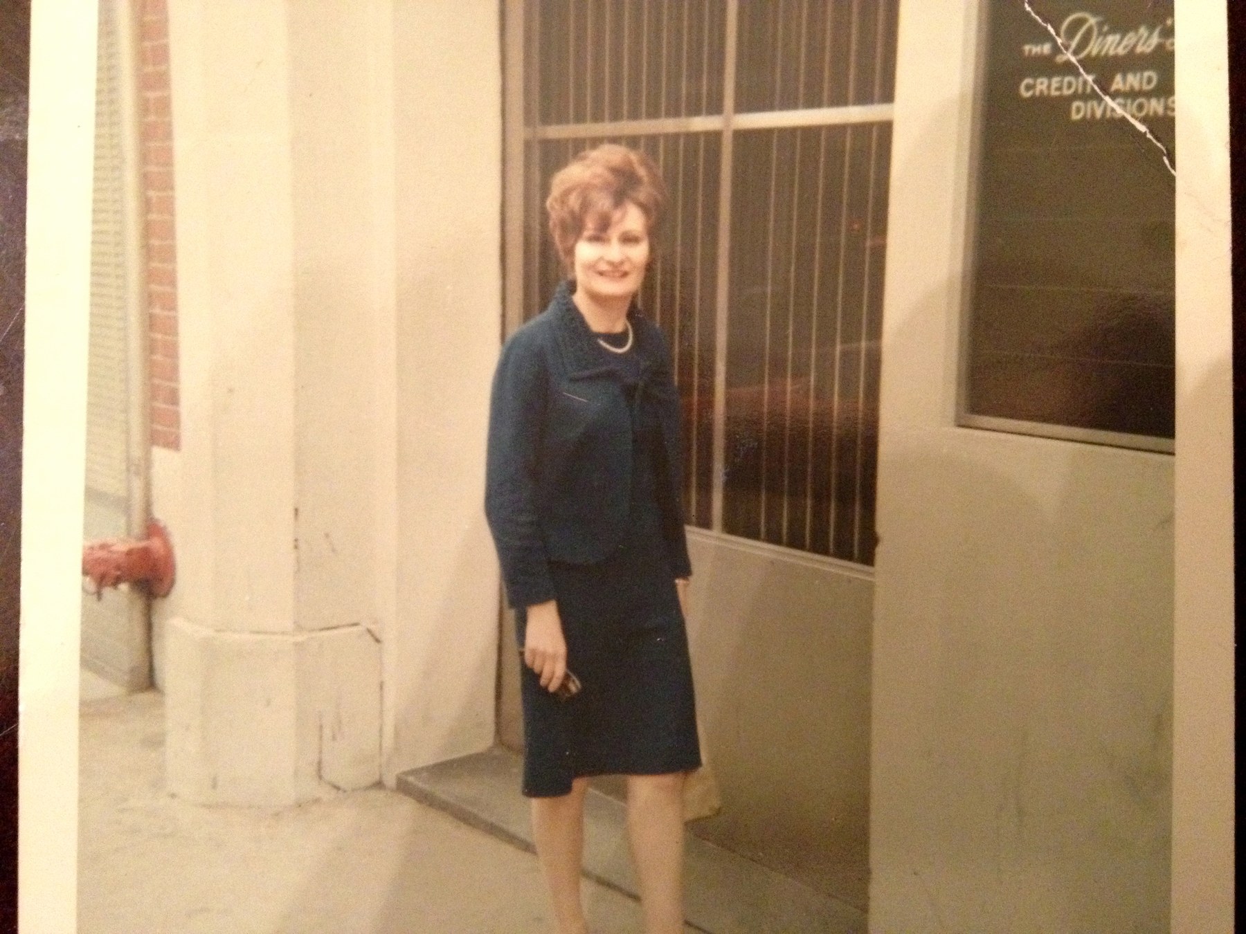 Maman standing outside an office building in a blue suit with pearls