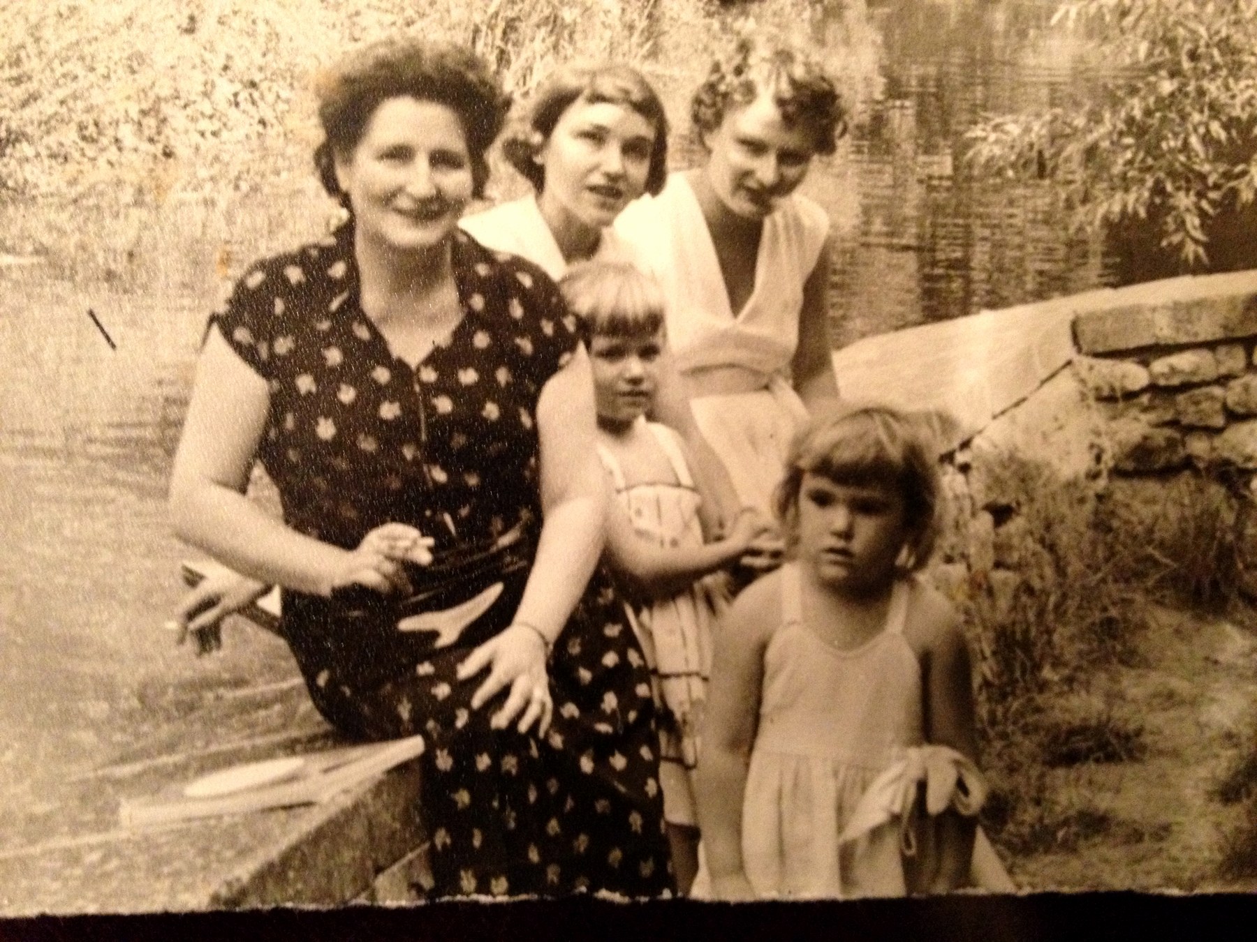A family group by a stone wall, two women standing behind an older woman seated, two small girls in front