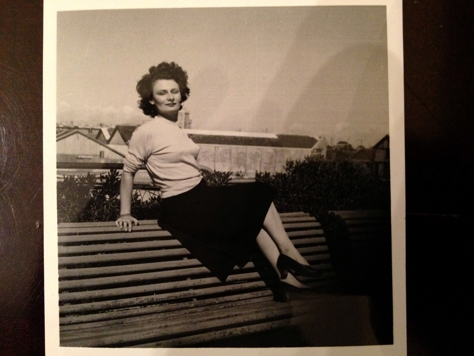 Maman as a young woman perched on a railing, rooftops behind her
