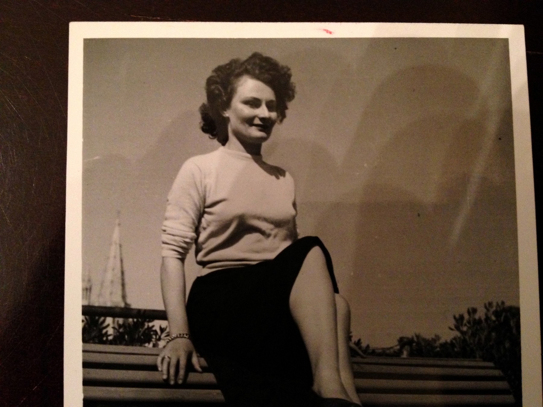 Maman as a young woman on a railing above a harbour, masts behind