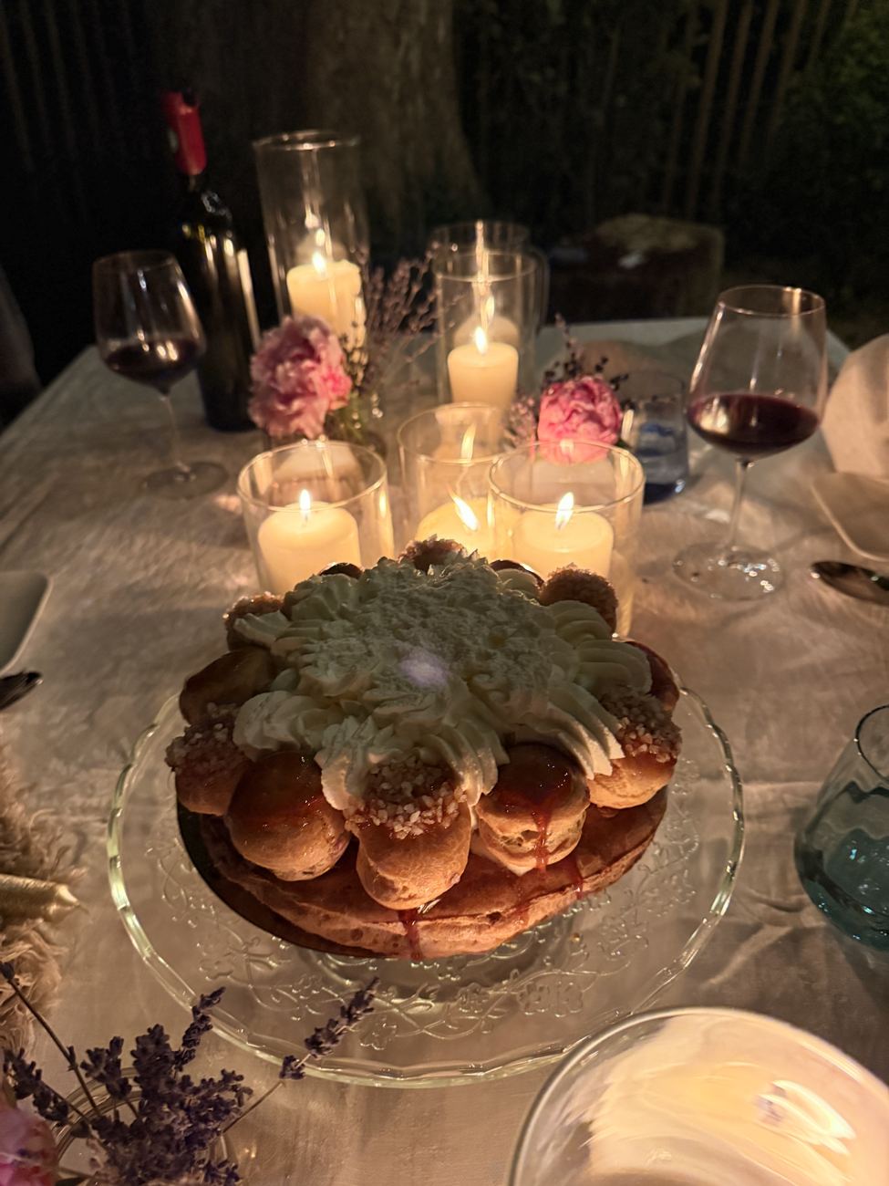 A tower of religieuse choux pastries topped with flowers and candles, on a candlelit table
