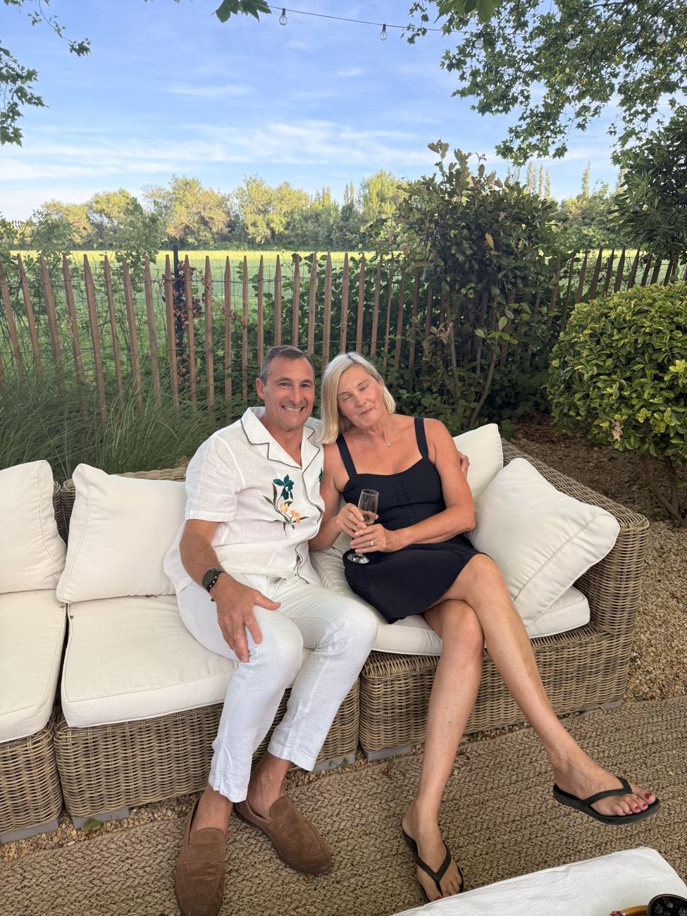 A couple relaxing together on a white garden sofa in the evening light