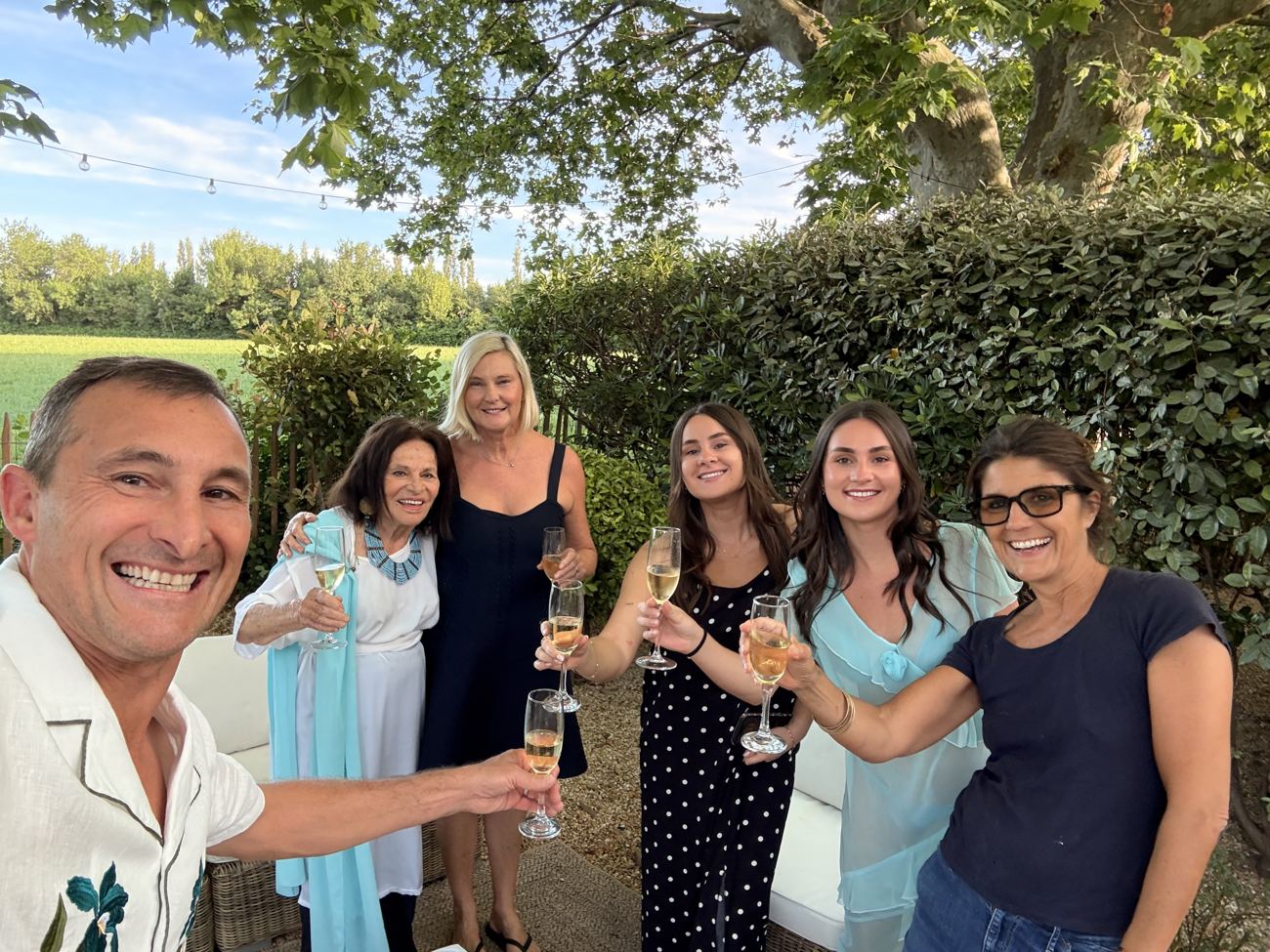 The family raising champagne glasses together in the garden at golden hour