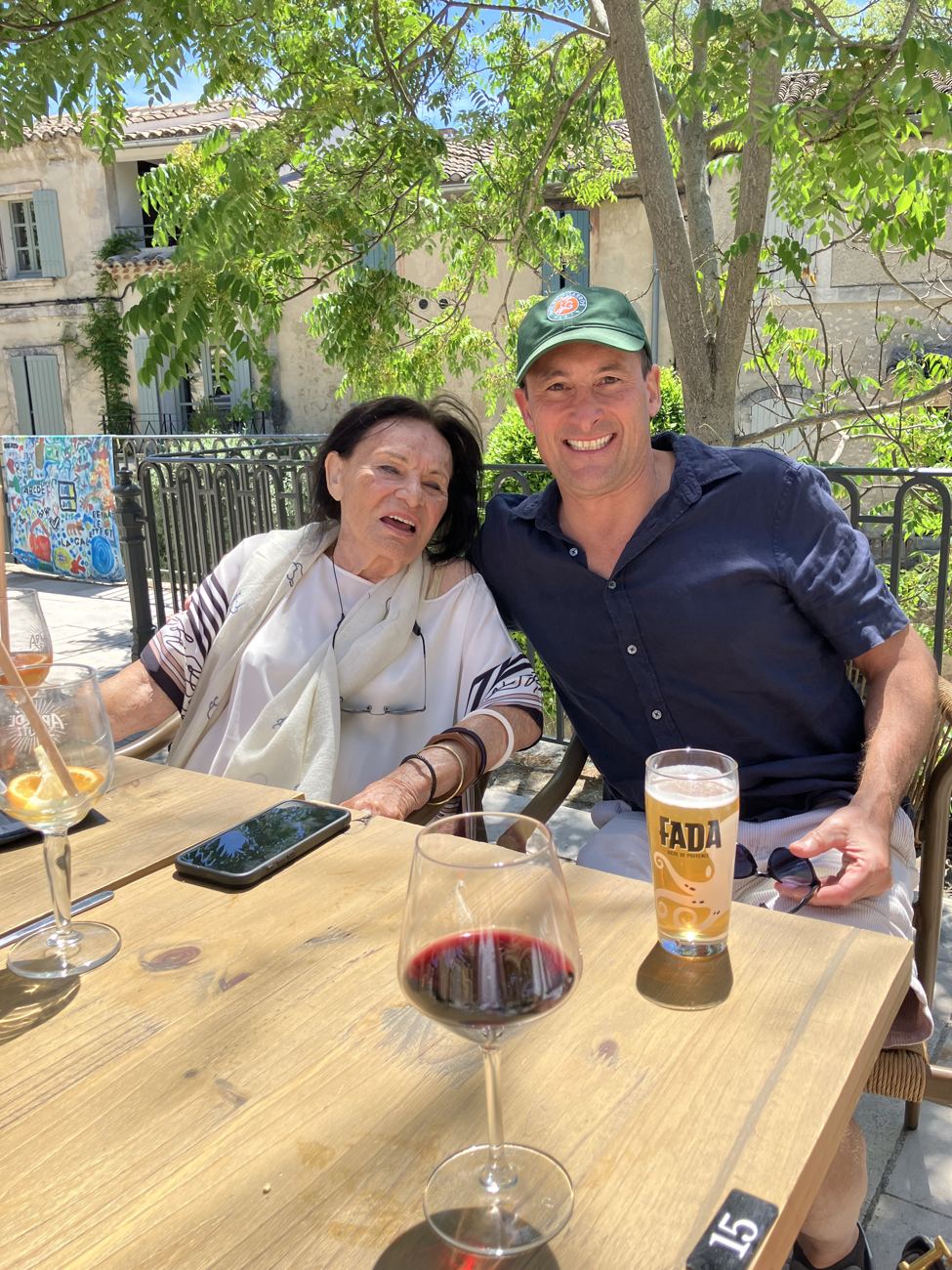 A couple at a shaded café table with a glass of red wine and a beer