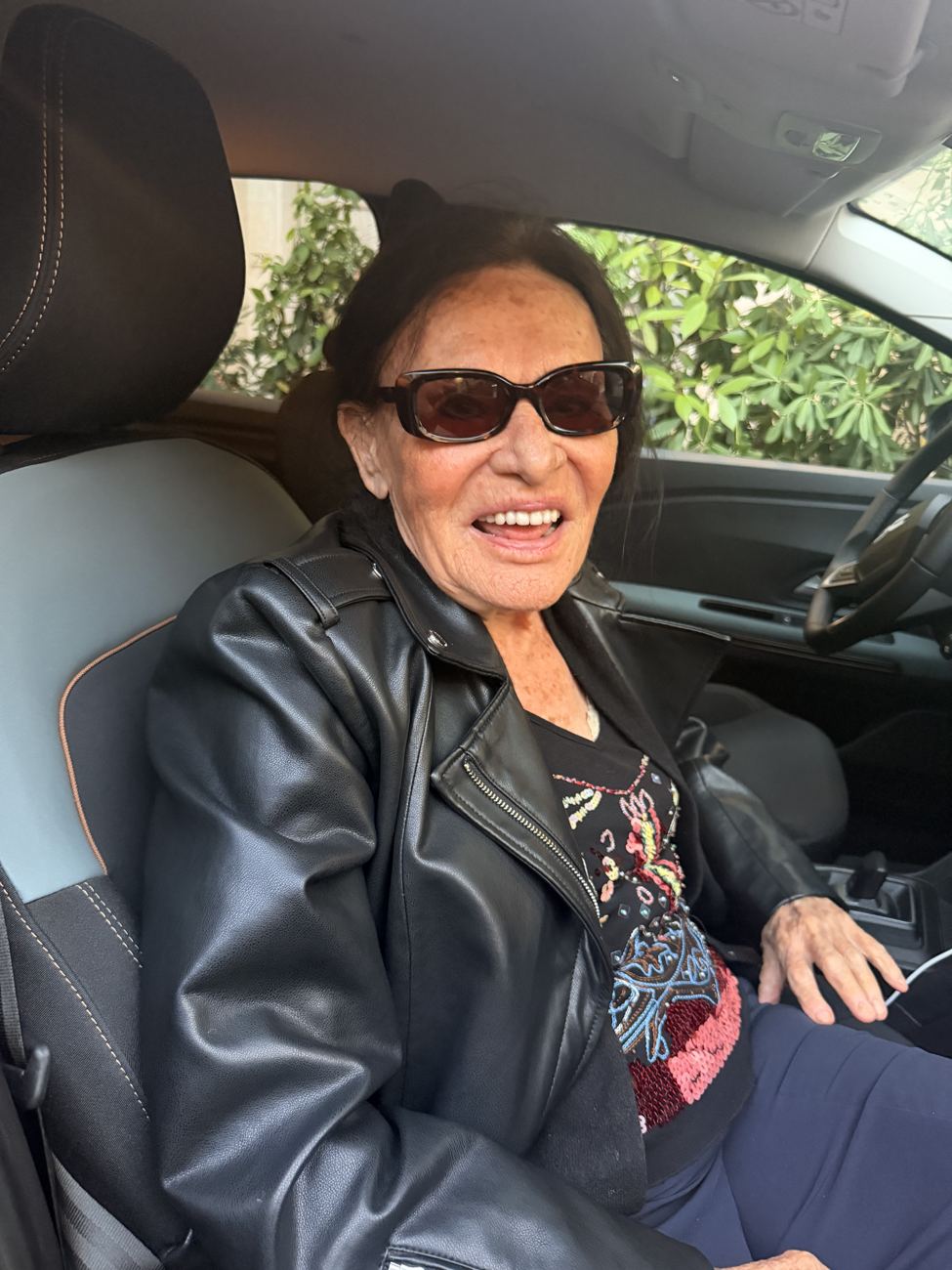 Maman in the passenger seat of the car, sunglasses on, the southern country sliding past the window